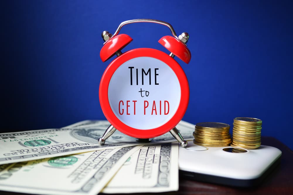 Red clock with a 'Time to Get Paid' sign, surrounded by money and coins.