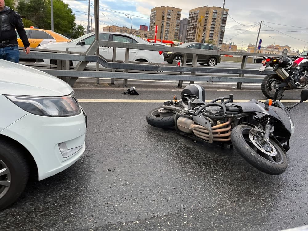 Motorcycle lies on slippery asphalt after crashing into car; accident involving motorcycle and car.