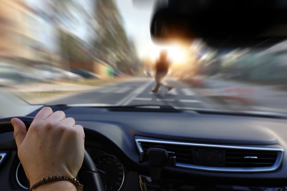 Pedestrian at a crosswalk with a distracted driver approaching.