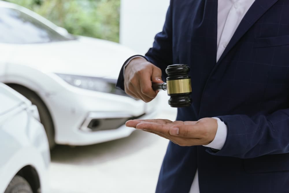 A person in a suit holding a gavel with two cars involved in an accident.