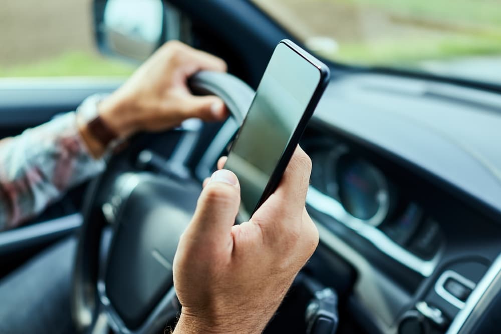 Man driving a car in the city while using a smartphone.