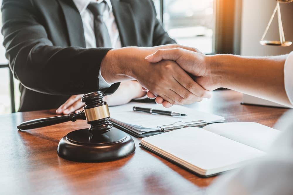 Businessman shaking hands to seal a deal in legal consultation with male judges and lawyers discussing contracts and case planning for court.