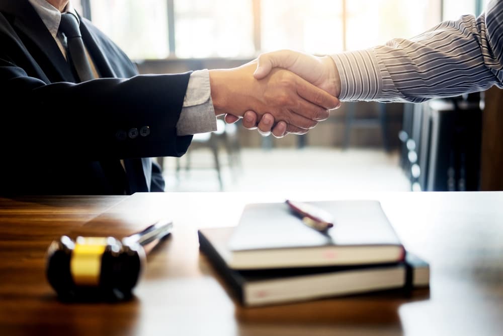 Judge's gavel on wooden table with judge and client shaking hands, lawyer service concept in courtroom background.