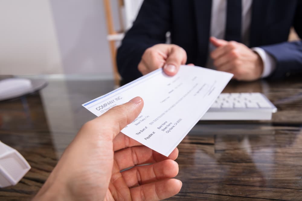 Close-up of an insurance adjuster handing a check to a colleague at their workplace.