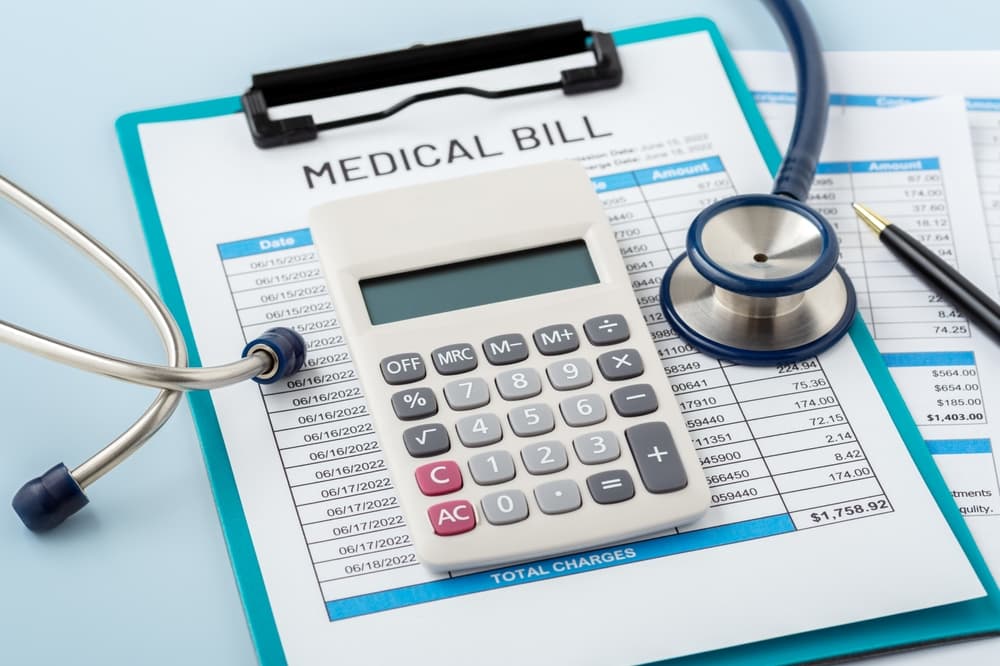 Calculator on a medical bill with a doctor’s stethoscope, representing healthcare costs and hospital payments, on a blue background.