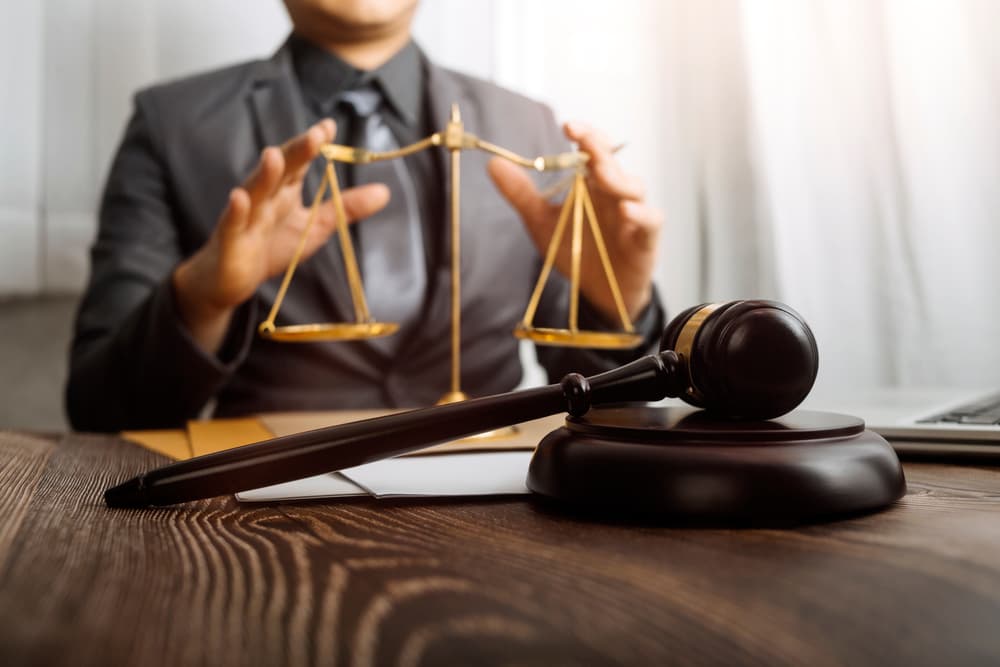 Lawyers reviewing contract papers with brass scale on office desk. Legal services, justice, and law concept with film grain effect.