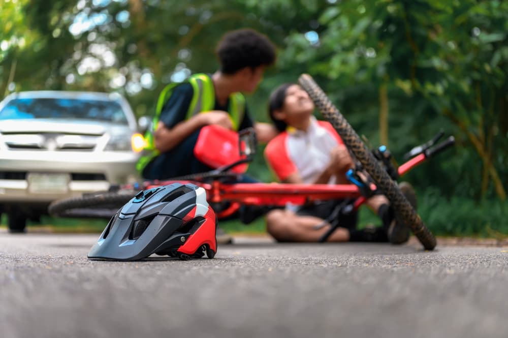 Two cyclists are involved in an accident; one is assisting the injured other.