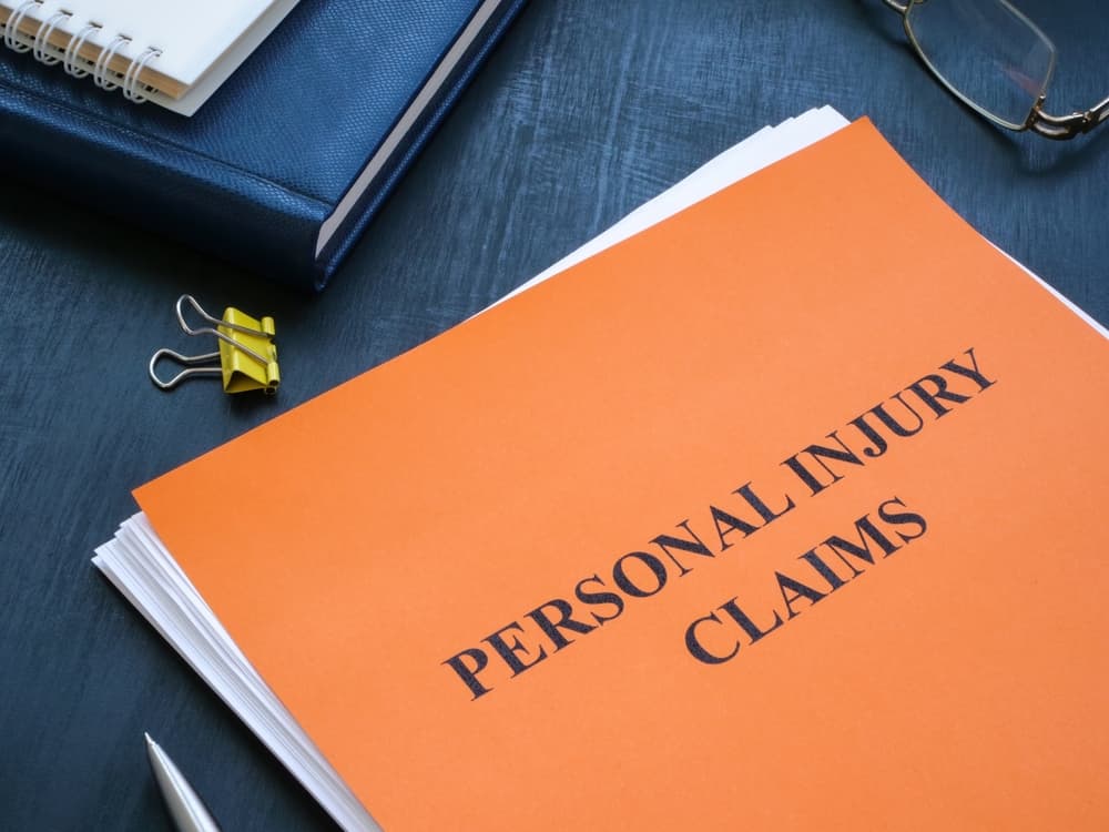 A folder labeled "PERSONAL INJURY CLAIMS" on a desk with a notebook, glasses, and a pen.