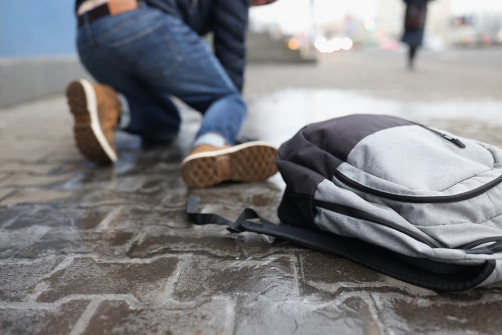 A person has fallen on a wet sidewalk, with a backpack lying nearby.