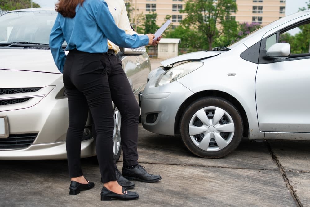 Two people standing between two cars involved in an accident, discussing and reviewing documents.