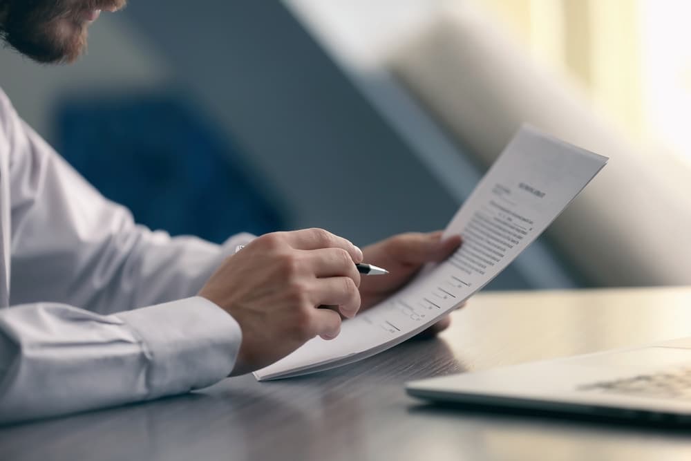 A person in a white shirt reviewing and signing a contract with a pen at a desk.