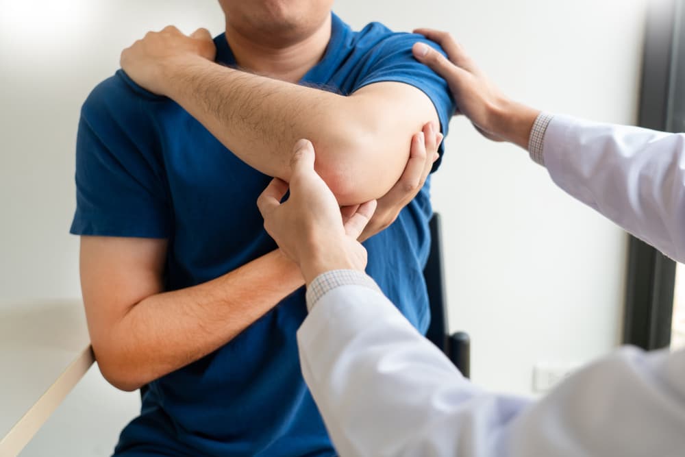 A doctor examining a patient's elbow during a medical consultation in a clinic setting.