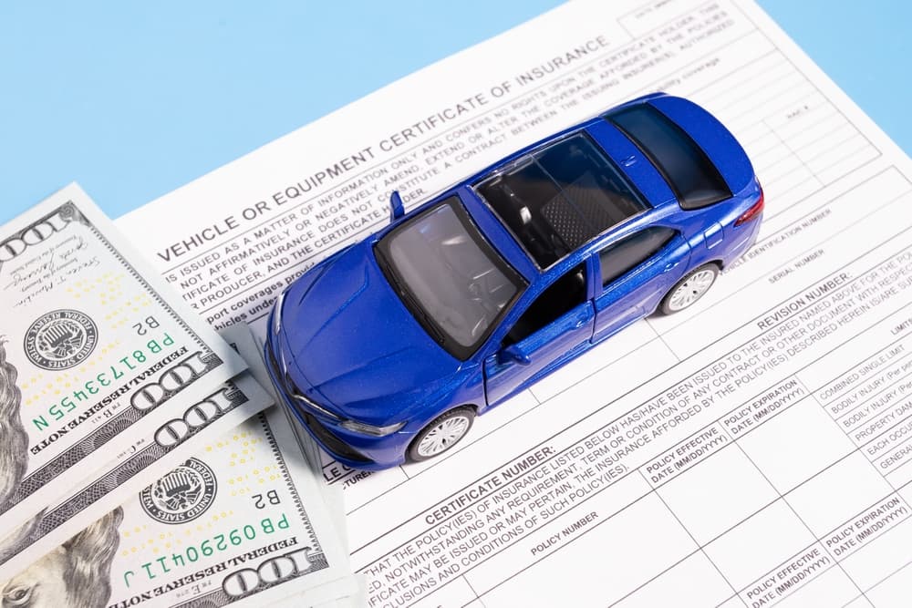 A blue toy car, dollar bills, and insurance documents representing vehicle insurance and compensation.