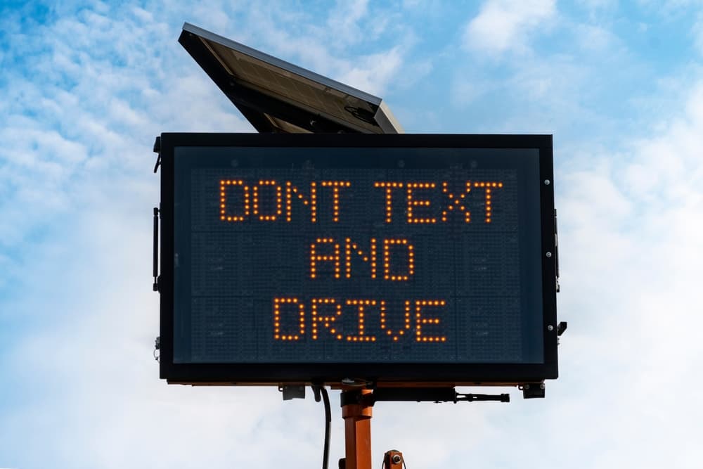 Electronic road sign displaying the message "DON'T TEXT AND DRIVE" against a cloudy sky.