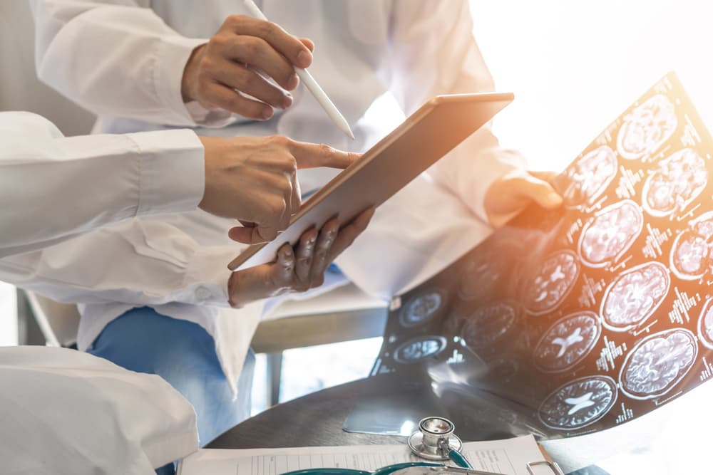 Doctors examining brain scan results while discussing on a digital tablet screen.