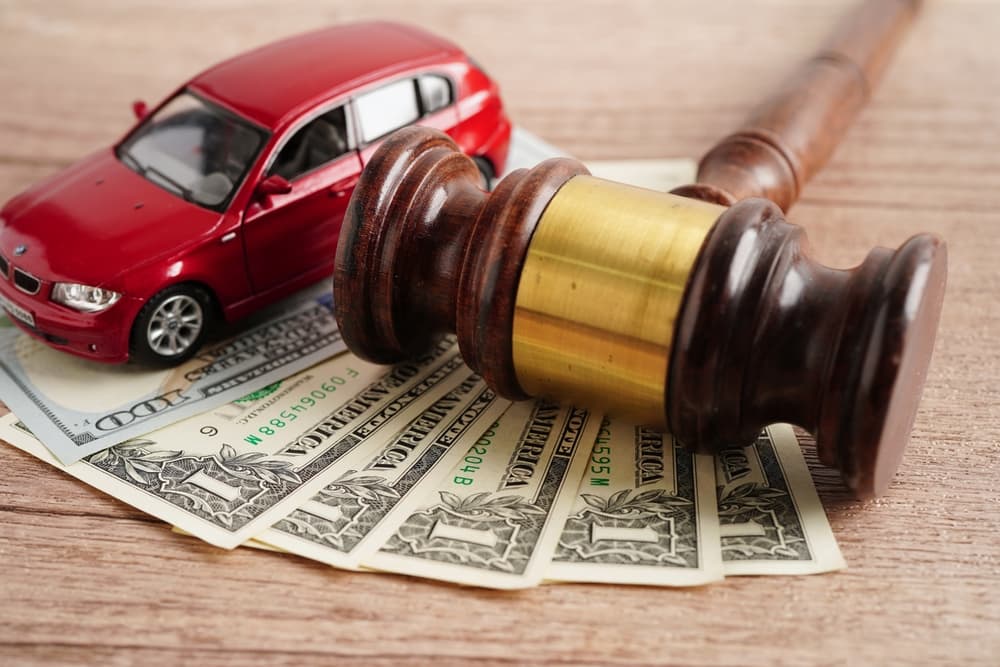 Close-up of gavel, red toy car, and cash symbolizing car accident legal and financial issues.