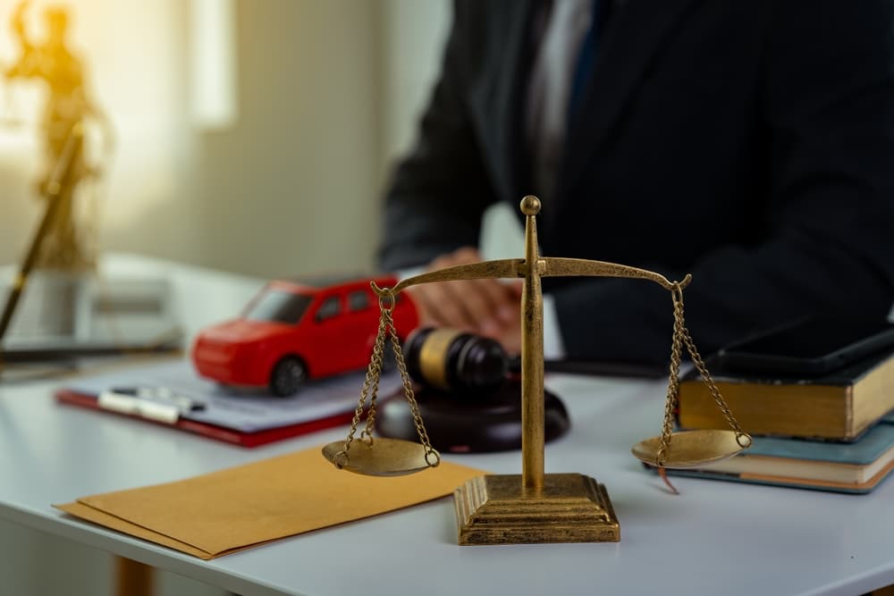 Close-up of justice scale on desk with lawyer, gavel, documents, and red toy car.