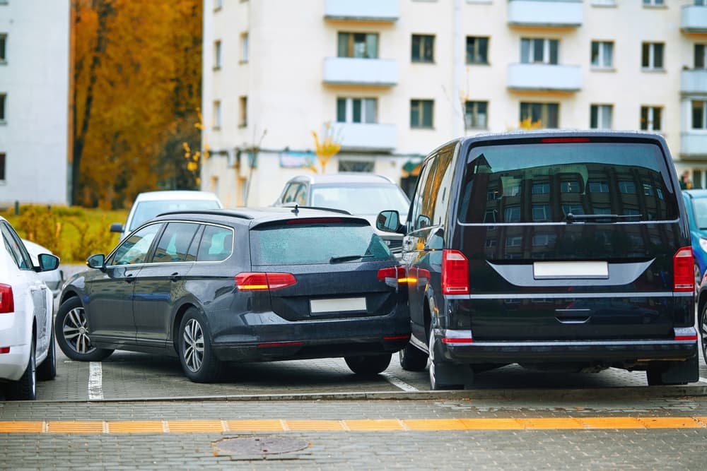 A parked car and a van have collided in a parking lot, causing visible damage.