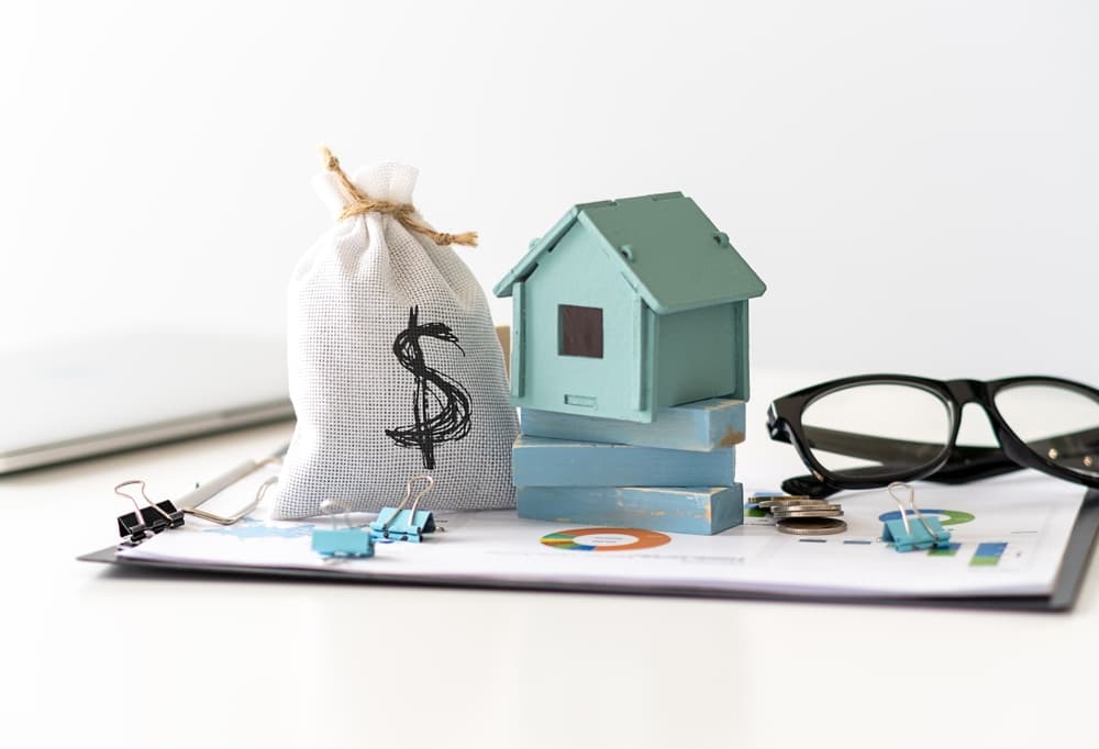 A money bag, model house, and documents with glasses symbolize finances and mortgage agreements.