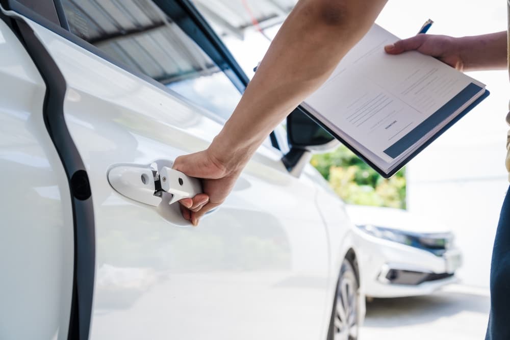 Person inspecting car damage while holding legal documents, likely preparing for a car accident lawsuit.