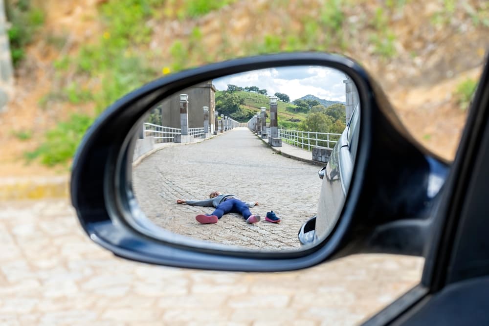 Fatal accident of a Pedestrian run over and lying dead on the road seen through the rearview mirror.